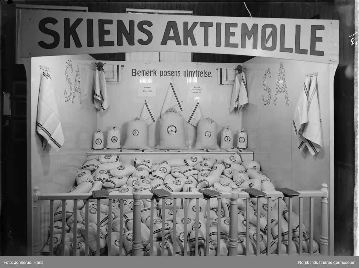Utstilling for Skiens Aktiemølle. Poser liggende innenfor gjerde, bøker på gjerdekant.