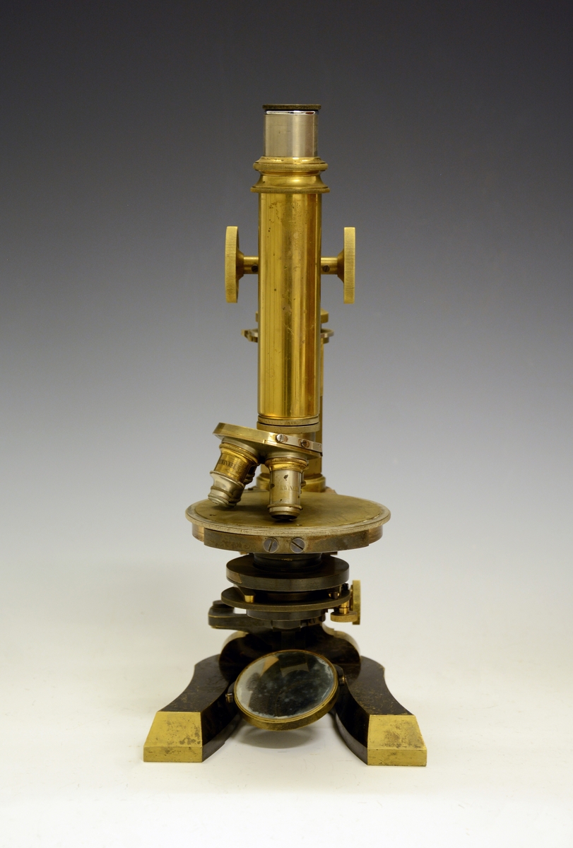 Mikroskop i kasse. Fra protokollen: Mikroskop. Stativet av massivt metall med hesteskoformet fot. Øverst på stativet røret (tubus) med objektiv og okular. Røret reguleres opp og ned ved drev og tannstang (grov innstilling). Bak røret skruehode for fin-innstilling. Mikroskopet har revolver med 4 forskjellige objektiver. Under disse bordet, som er en dreibar sirkulær skive med hull i midten hvorigjennom det sendes lys gjennom objektet fra et belysningsapparat under bordet. Nederst et dreielig plan- og hulspeil, over dette er blender som reguleres med tannstang og drev. Over blenderen kondensor med linser. På ryggen av stativet er inngravert: "No 1856 R. Winkel Göttingen 1891". Mikroskopet er plassert i et treskap med sidehengslet dør som har lås (nøkkelen mangler) og metallhandtak på toppstykket. Inni skapet og på innsiden av døren profilerte treknotter foret med filt, som holder mikrioskopet på plass. Profilerte lister (skinner) bærer et penalhus av tre med skyvelokk, en foret og trukket tre-eske som har et toppstykke med 5 hull (Esken er merket "E. Leitz, Wetzlar") og øverst en treplate med 3 større og 2 mindre hull. På toppen av døren mrk. "132986". Løst inni skapet en kondensor og en metallhylse.