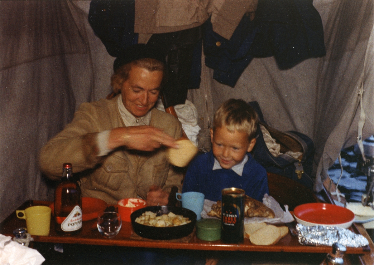 Måltid i sittbrunnen på segelkanoten UNDA sommaren 1961. Mahognylocket till lådan med köksutrustning är placerad tvärs över båten och tjänstgör som bord.