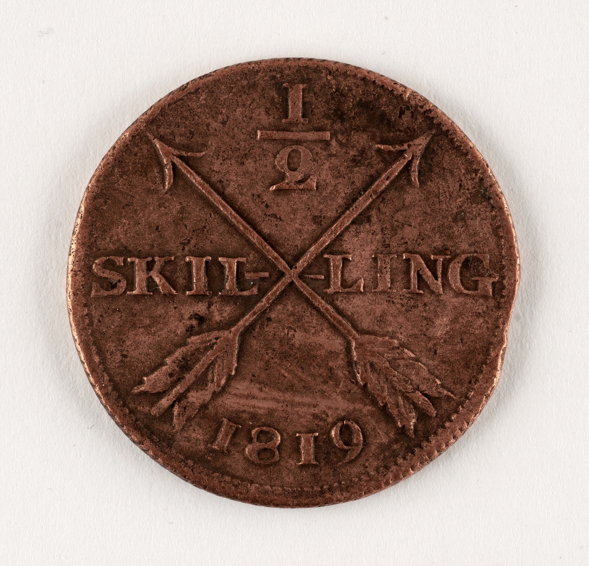 Präglat mynt, av koppar. 1/2 skilling. Åtsida; tre kronor, myntherrens krönta initialer:
C XIV samt omskrift: FOLKETS KÄRLEK MIN BELÖNING. Frånsida: två korslagda pilar samt texten: 1/2 SKILLING 1819. 
Mindre skador.