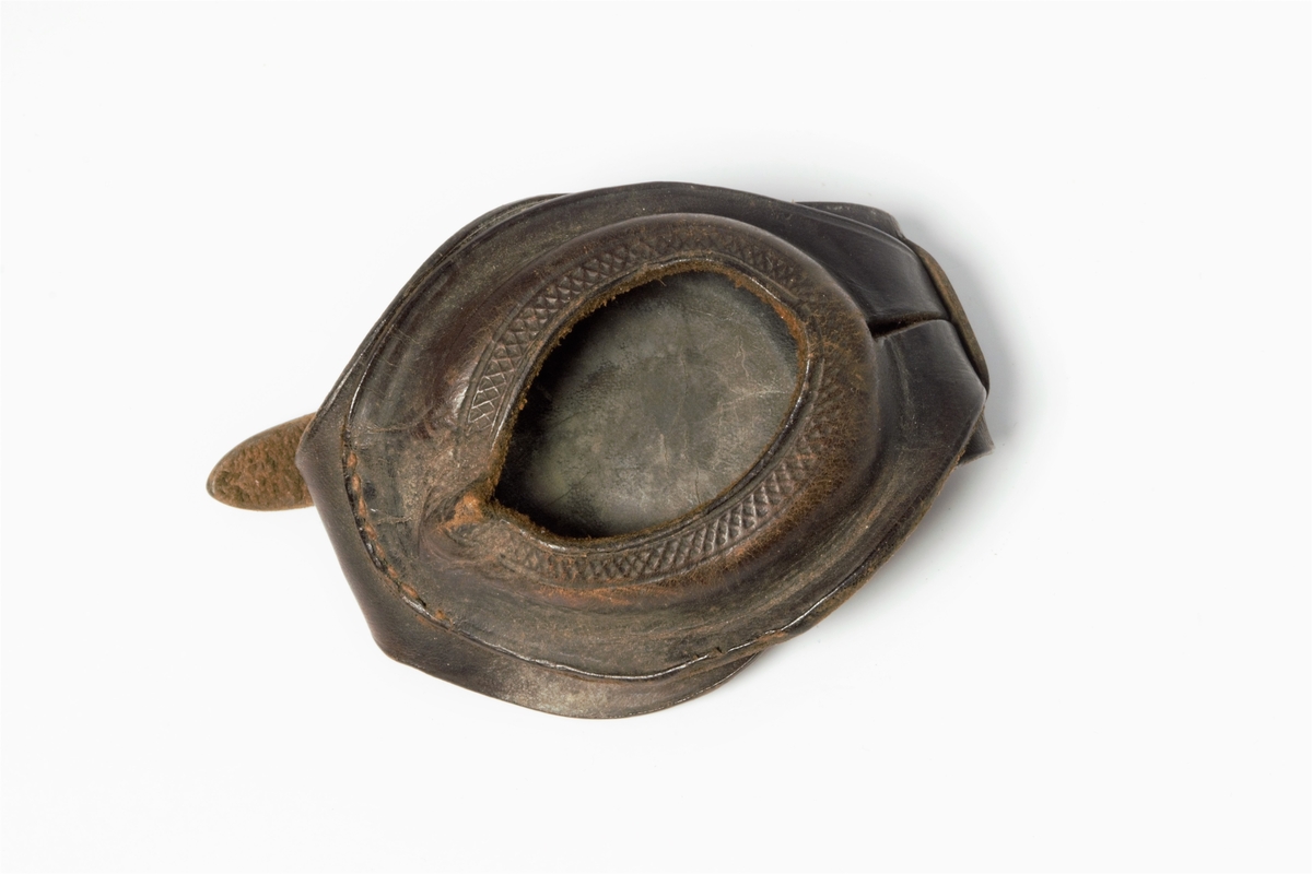 Klokkereim som er skåret til med oval fasong midt på. To deler som er sydd sammen. I hver ende er det reimer, den ene med spenne av metall og i den andre enden er det fem justeringshull. Lite rom til å plassere uret under slik at bare urskiven viser. Dette dannes ved at de to delene på den ene siden blir tredd i hverandre, og kan åpnes på den måten. Dekorert kryss som danner en bord langsmed hullet til klokka.