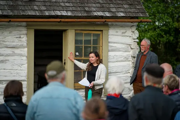 Kvinne står utenfor en bygning i friluftsmuseet og formidler til et publikum.
