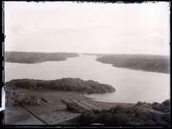 Landskapsbild. Odling i förgrund. Hav i centrum. Klippor i b