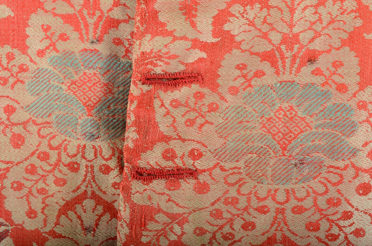 Materiale: Tofarga ulldamask med brosjering (kallemank) i 2-
tråds tynt ullgarn. Bunnen er i ubleika og rødorange og
brosjeringer er i gult, mørk blått, lys gråblått og gulgrønt.
Vesten er helfôra med grovt linlerret. Lommefôr av samme
linlerret. Snitt: sein rokokko ? Framstykkene er dobbeltknept
med 9 knapphull og merker etter 9 knapper på hvert stykke. På
høgre framstykke er det igjen de to øverste knappene.
Knappene er festa med skinnreim. Knapphullene er sydd med
rødorange 2-tråds ullgarn. Regels i begge endene. Framkanten
er rett, men like nedenfor er det nederste knapphullet er
kanten skrådd. Nedrekant av framstykket buer svakt nedover
mot framkanten. Ei klaffelomme nede på hvert framstykke.
Ekstratekst. Øvre del av klaffen ligger omtrent i flukt med det
nederste knapphullet. Isettingssømmen for klaffen buer
oppover mot sidesømmen. Klaffen ligger ca 3 cm fra sidesøm.
Lomma er grunn. Sidesømmene er bakovertrekt, svakt buede
og med åpne flasker nederst. Framstykkedelen av flasken er
sidere enn bakstykkedelen. Ryggsøm midt bak med åpen
flaske nederst. Ryggstykkene skrår innover ned til starten på
flasken. I sjølve flasken skrår stykkene utover. Skuldersømmene
er bakoverstrkte og skrådde. Skjøt ved høgre skuldersøm.
Runda halsringing. Smal tittekant i halsringingen mellom fôr
og hallemank på bakstykkene og fram til omtrent rett opp for
knappefestet. I midt bak sømmen er fôr og hovedstoff sydd
sammen hver for seg, trolig med atterstin. Sidesømmene er
sydd sammen som spilesøm. Langs ytterkantene er sårkant på
fôr og hovedstoff bretta inn og fôret er sydd ned til
hovedstoffet med faldesting som vises som prikkesting på
retta. Fôret ligger ca 2 mm inn fra kanten til kallemanken og
opp langs skråkanten framme (til nederst knapphullet) er det
sydd ei ektra prikkestingsrad ca 9 mm inn fra kanten. I
skuldersømmene er fôr og hovedstoff sydd sammen hver for
seg med attersting. Alt sømmonnet er bretta bakover og det er
sydd ei prikkestingsrad på retta.
