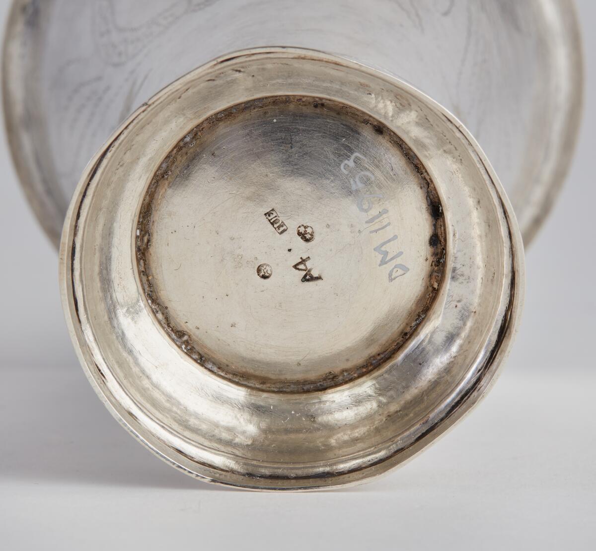 Bägare, silver, med utsvängd, profilerad fot, vidgad uppåt med utvikt kant längst upp. Bägarens övre del försedd med dekor av vinkelböjd ranka, därunder bred blomranka med bl.a voluter och "OOS" inom blomkrans. Även den utsvängda foten dekorerad. På bägarens botten stämplar: "FUE", "A4", trekronorsstämpel, Falustämpel. FUE=Fredrik Ulrik Ekholm. A4=1831.

Från Västbergs by, Rättvik, se bilaga.