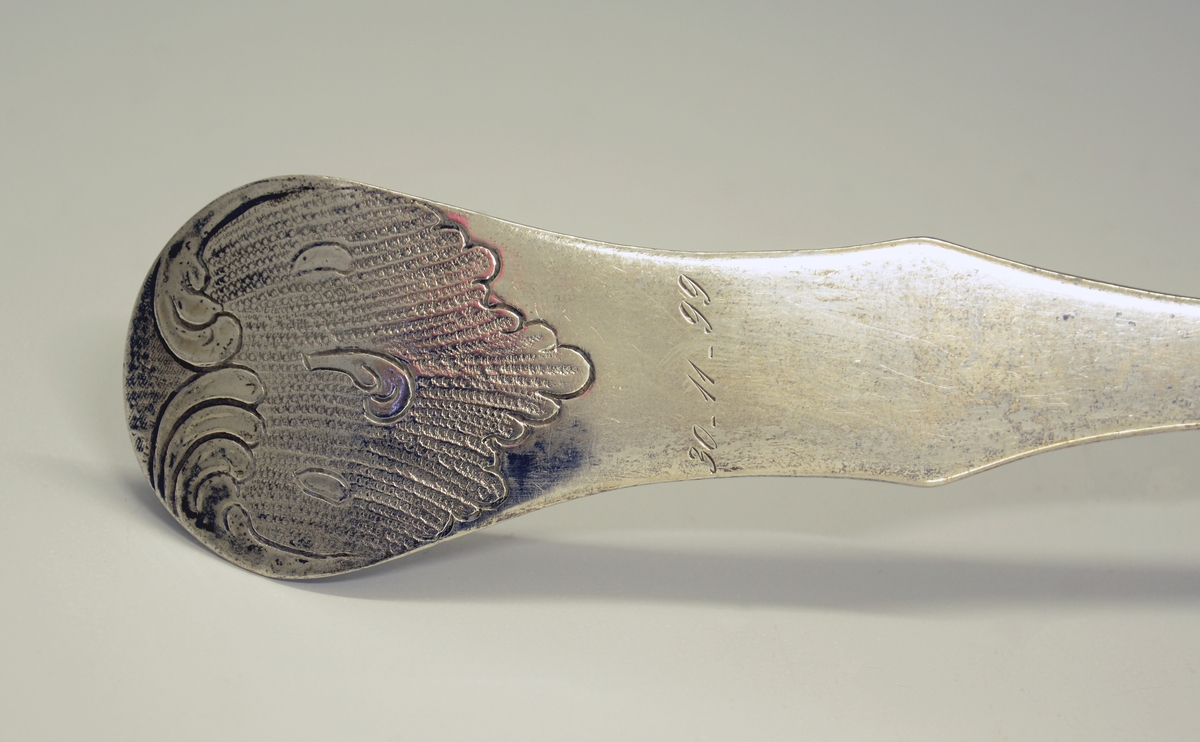 Sølv suppeøse. Dekorert med rokokko-ornamenter. Stemplet med København bystempel og ant. året 1779. (Tre tårn og 79), månedstempel for væren (20.03-20.04), guardeinstempel "F" ant. for Fredrik Fabricius ((1767)1787-1823, København) og mesterstempel PM.