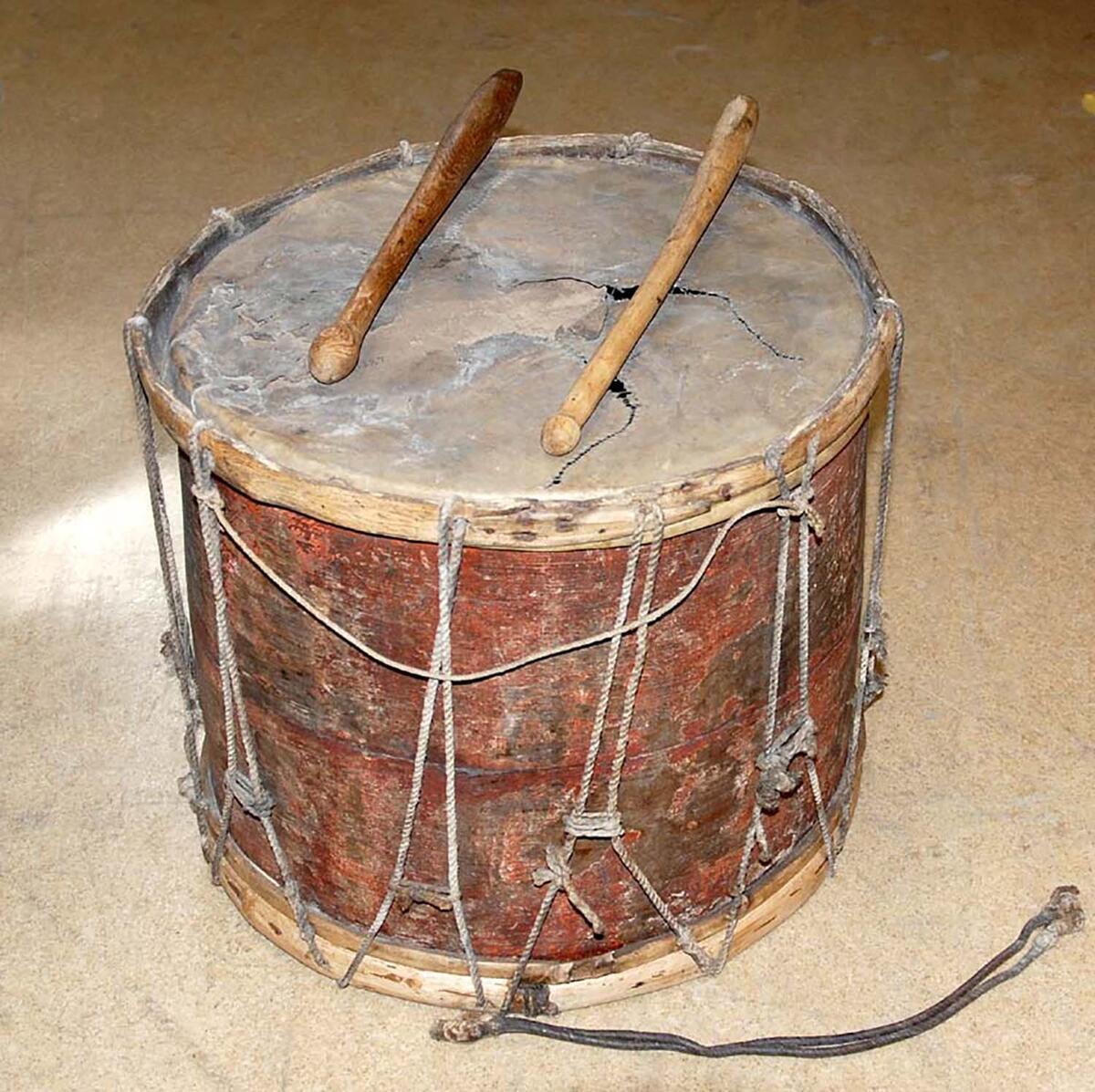 AV TRÄ, HÖJD OMKR. 39 CM. TVÄRMÅTT 44 x 46 CM; MÅLAD RÖD. (SKINNEN KONSERVERADE VID MUSEET). HAR TILLHÖRT KAPELLET I HALLSHUK. ENLIGT SÄVES:  "HAFVETS OCH FISKARENS SAGOR", ( ANDRA UPPLAGAN SID. 61), TRUMMADES FOLKET SAMMAN, DÅ KYRKOHERDEN I HANGVAR PREDIKADE TVÅ SÖNDAGAR OCH STADSKAPLANEN I VISBY DEN TREDJE UNDER FISKETIDERNA, VÅR OCH HÖST. ENLIGT UPPGIFT AV KYRKOVÄRDEN, J. HÄGVALL I HÄGVARDS, (GENOM FOLKSKOLLÄR. N. HALLÉN) ANVÄNDES TRUMMAN MORGON OCH AFTON FÖR SIGNALERING, "OM MORGONEN FICK FISKAREN EJ BEGE SIG UT PÅ HAVET, FÖRRÄN TRUMMAN GÅTT, OM AFTONEN SKULLE HAN VARA HEMMA, DÅ TRUMMAN GICK".