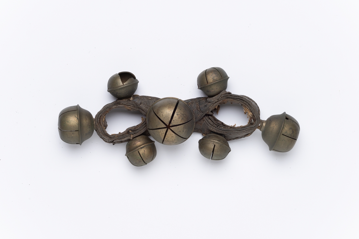 Bøyd lærrem (8-tallsformet), påsatt 7 kuleformede hule metallbjeller i forskjellige størrelser. Bjellene har spalter og innlagt kule som klirrer når den rister. For plassering oppå bogtrærne.