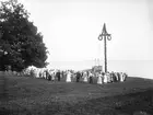 Midsommardans vid Korsvik invid sjön Roxens norra strand. Vid bryggan ligger Thora med hemmahamn Linköping och som lövad skeppat firare från staden. Året var 1903.