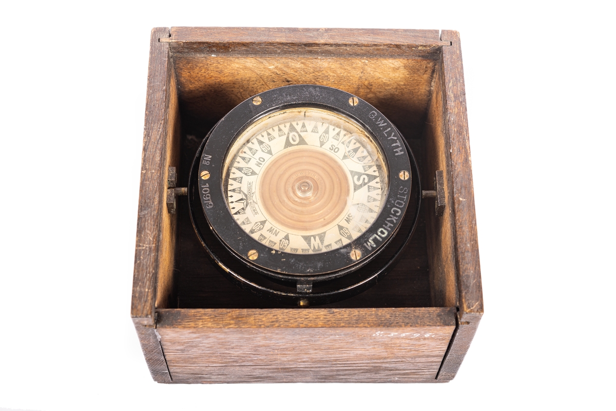 3,5 tums båtkompass, graderad i interkardinalstreck och 5 grader. Kardansk upphängning med röda tappar. Fyrkantig låda av ek med skjutlock.