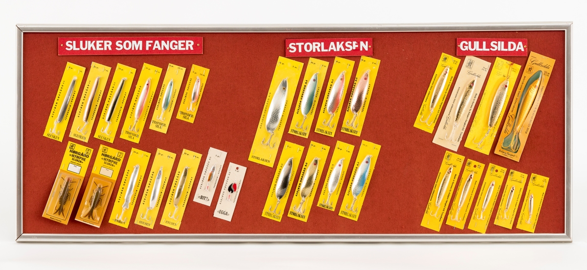 30 sluker med modellbetegnelsene "Slusken" (3 stk), "Trøndersila" (3 stk), "Nymphesluken" (2 stk), "Sniken" (1 stk), "Snusen" (2 stk), "Bitt" (1stk), "Egga" (1stk), "Storlaksen" (8 stk) og "Gullsilda" (9 stk) er montert på en innrammet sponplate. Sponplata er overtrukket med rød filt og innrammet med søvlfargete trelister. Øverst, midt på plata, er det 3 skilt med tekstene: "Sluker som fanger", "Storlaksen", "Gullsilda". På baksiden er det oppheng for feste til vegg (utstillingstablåer). Slukene er produsert av firmaet Asbjørn Hørgård A/S i Trondheim. Alle slukene som er montert på plata ligger i originalemballasje: papplater med påtrykt produktinformasjon overtrukket med plast. 

Alle metallslukene er utstyrt med treblekroker (trippelkroker) festet til splittringer. Nymphesluken har dobbeltkrok

I produktkaktalogene "Råd og redskap fra Hørgård" er flere av slukmodellene omtalt. Omtalene av disse gjengis her: 
"Trøndersila": "En av våre beste allrond sluker. Vektene 7 - 12 - 20 gr gir  Dem gode muligheter for variert fiske i vann, elv og sjø. Gull, sølv, kopper.  7-12 gr. kr. 4 ,70  20 gr 4, 90". (1972).

"Storlaksen": "Stor stri elv - nygått laks - hugg - kamp ... De vet hva De må bruke: Stor, tung sluk, halvblank sølvfinish med kopper innside. Da har De storlaksen! Til dorging i sjøen er den også en stor fisker. 45 gr kr, 8,30 28 gr kr. 7,30". (1972)

"Sniken": "Den lett vrikkende gang i vannet gjør den til et fristende bytte for større fisk. Best til laks og sjøfiske. Farger: Gull, sølv. 24 gr. kr. 4,90". (1972)

"Sluksen": "Langstrakt form og rikelig refleksi ryggens mønster. Særdeles god til elvefiske og sjøfiske. Gull-sølv-kopper 20 gr. kr. 5,20" (1972)

"Gullsilda": "Formen er den samme som på Stingsilda - sannsynligvis Norges mes solgte sluk. Denne silda er belagt med rent gull. Ikke så mye riktignok, men nok til å gi en helt spesiell lysreflekterende gullfarge, som virker tiltrekkede på fisken. Priser: 7g/47 mm kr. 9,30, 12 g/ 55 mm 9,30, 18 g/ 66 mm kr. 10,10, 28 g/ 80 mm kr. 12,20, 40 g/ 90 mm kr. 13,70, 60 g/ 100 mm kr. 15,10, 75 g/110 mm kr.19,80 (Priser i 1981) 

"Nymphesluken 10 gr.": Gummiimitasjon. "Imitasjon av en døgnflue på et bestemt utviklingstrinn. Best kjent som flue og opphenger, hvor den har vist meget gode resultater. De gode rapporter fra testing og de som har kommet inn i år (1981) har også vist at den er en god som sluk. Bør fiskes rykkvis enten ved å vippe stangtoppen, eller å sveive inn med ujevn gang. Da imiterer man best den naturlige nymphen. For lengere kast og dypere gang, kan en eller to spesalbygde blykuler, hver på 7 1/2 g., trees inn på snøret foran sluken. Pris. kr. 13,90" (1981)

"Egga": "En artig liten ørretsluk som under prøvefiske har vist meget gode resultater. Men den bør fiskes langsomt. Farger: Gull, sølv og kobber. Alle med dekor i dyp blågrønn/rød. Vekt: 5 g. Pris: kr. 9,90" (1981)

"Bitt": "En lett sluk med riktig gang. Bruk den etter ørret eller annen fisk. Vekt: 5 g. Pris: kr. 8,70" (1981)



[Se fanen Opplysninger for informasjon om Asbjørn Hørgård og hans firma.]