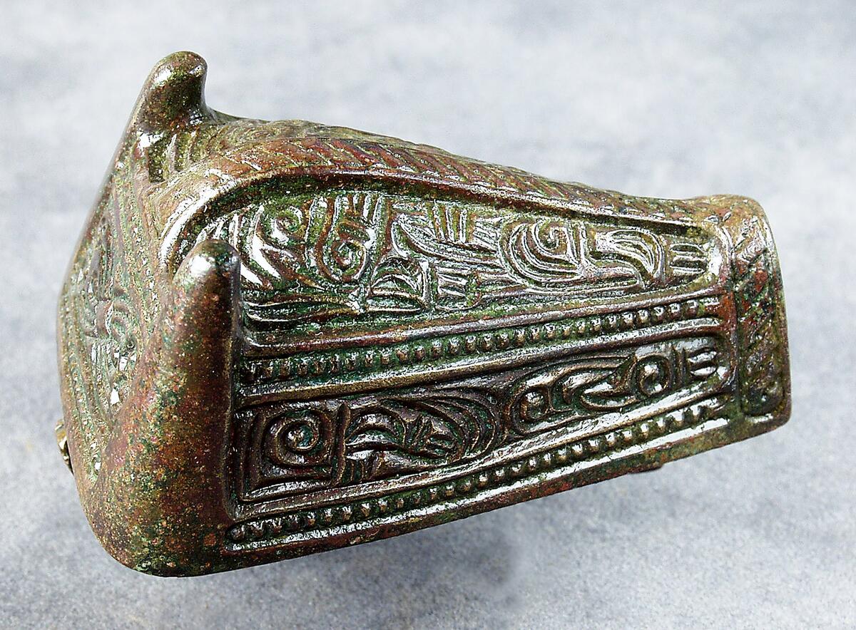 Djurhuvudformat spänne av brons. Gjutet i ett stycke, plan bottensida med nål. Ovansidan med huvudsakligen nonfigurativ ornamentik, + 4 hartsklumpar. Påträffad  i grav 141/64 på kopparsviksgravfältet söder om visby.  Publ. Pettersson h 1966 (mälarstedt) undersökningen av gravfältet vid kopparsvik, gotländskt arkiv. Mälarstedt h 1979 kopparsvik- ett vikingatida gravfält vid visby. Arkeologi på gotland
nyreg 2002 ml