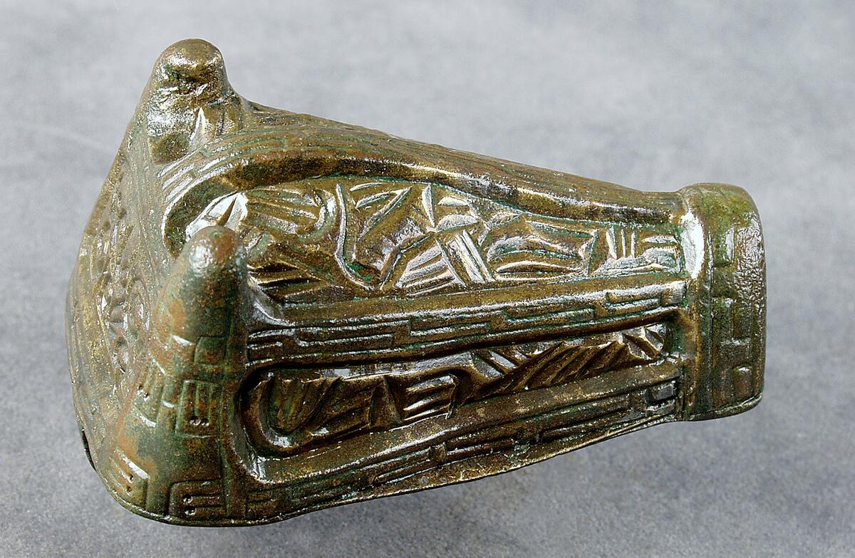 Djurhuvudformat spänne av brons, undersidan med pånitad nål på ovansidan ornamentik i relief. Påträffad i grav 232/64 på kopparsviksgravfältet söder om visby.  Publ. Pettersson h 1966 (mälarstedt) undersökningen av gravfältet vid kopparsvik  gotländskt arkiv. Mälarstedt h 1979 kopparsvik- ett vikingatida gravfält vid visby. Arkeologi på gotland.
nyreg 2002 ml