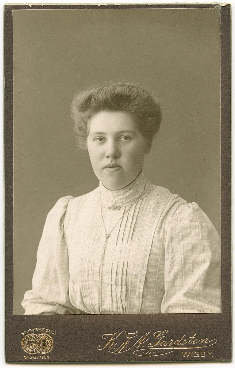 Svartvitt fotografi av kvinna i vit blus av krelskiftesmodell (1900) i bordsram dekorerad med snäckor, några helt bortfallna andra lösa men bevarade,
nyreg data 010404 li