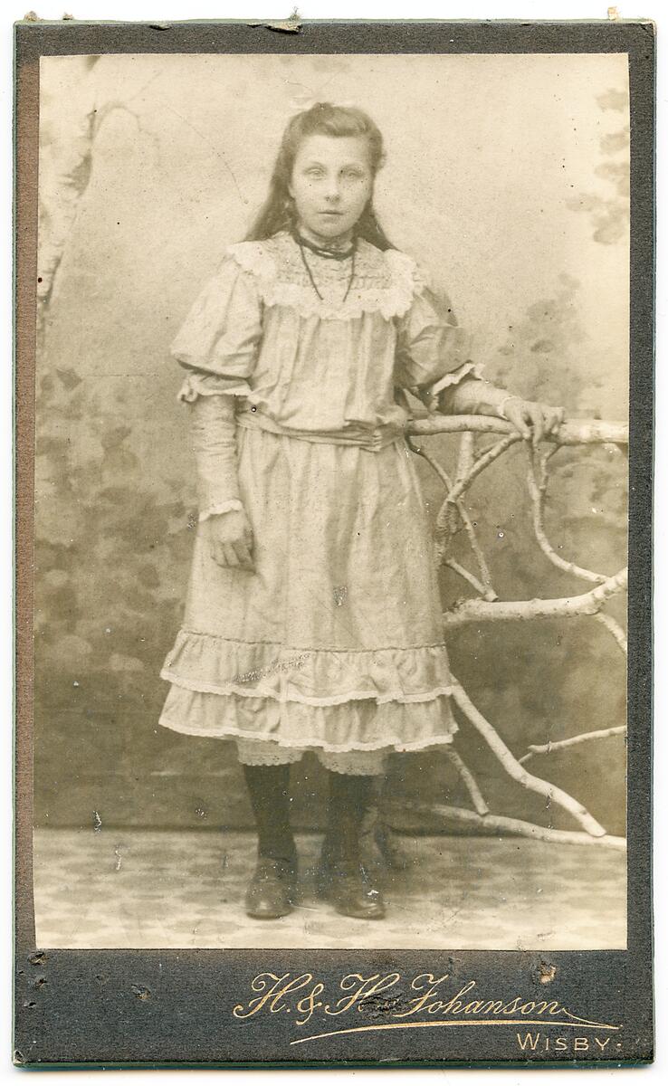 Inramat svart-vitt fotografi som föreställer en flicka, rikt dekorerad ram av papp med snäckor som dekor, en del snäckor har lossnat, se inventnr gfc14317_2 samt gfc14302.
nyreg Data 010330 ks