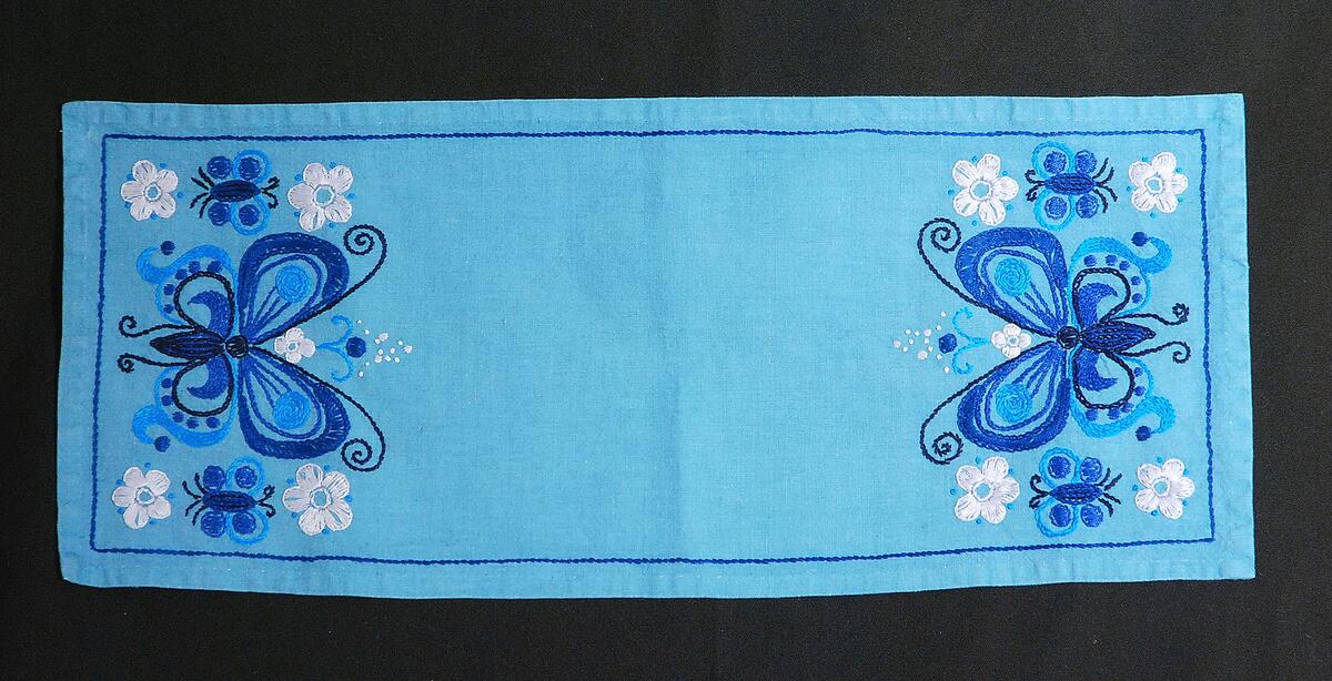 Avlång blå duk med broderade fjärilar i blått och blommor i vitt
Nyreg 010827 TL