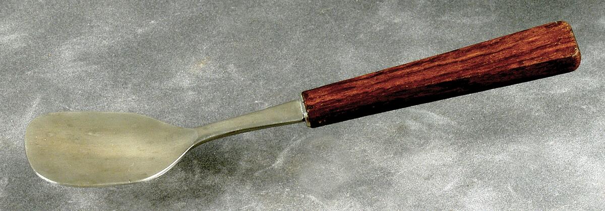 Sked till uppläggningsfat, endast svagt skålad, i rostfritt stål med handtag i mörkt trä, märkt undertill "18-8 stainless steal". Förvaras tillsammans med tillhörande uppläggningsfat i originalask med pappersbotten och genomskinligt plastlock. Skeden och fatet hör till ett set med sex stycken fruktknivar i ett ställ under huvudnummer 14942, för information om dödsboet se inventnr gfc14302.
nyreg 020121 jt