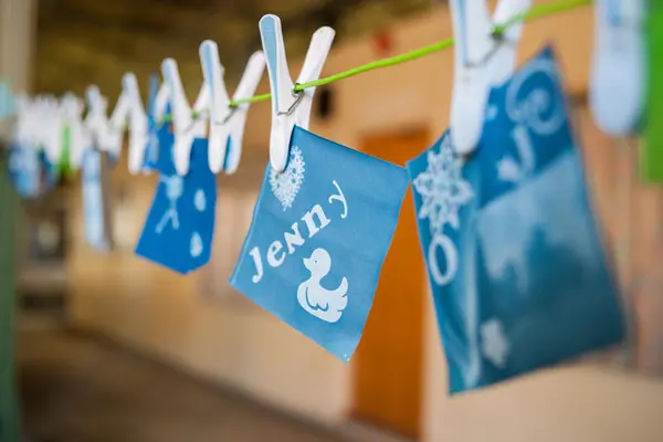 Blått papir med hvite illustrasjoner henger med klyper på en snor. Fotografi.