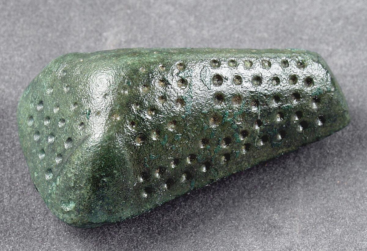 Litet djurhuvudformigt spänne, ornerat över hela ytan med punkter. Bevarad botten i ett med överdelen, nål saknas. Skadat med ett hål på ena sidan, enligt orginalkatalogen  funnen i milåker vid lundbjers i lummelunda.
djurhuvudformad, 44 mm. Lång. (torn saknas), litet hål å motsatt sida som figuren visar, se original.kat.c. Hnr: 864. Funnen i milåker vid lundbjers i lummelunda.