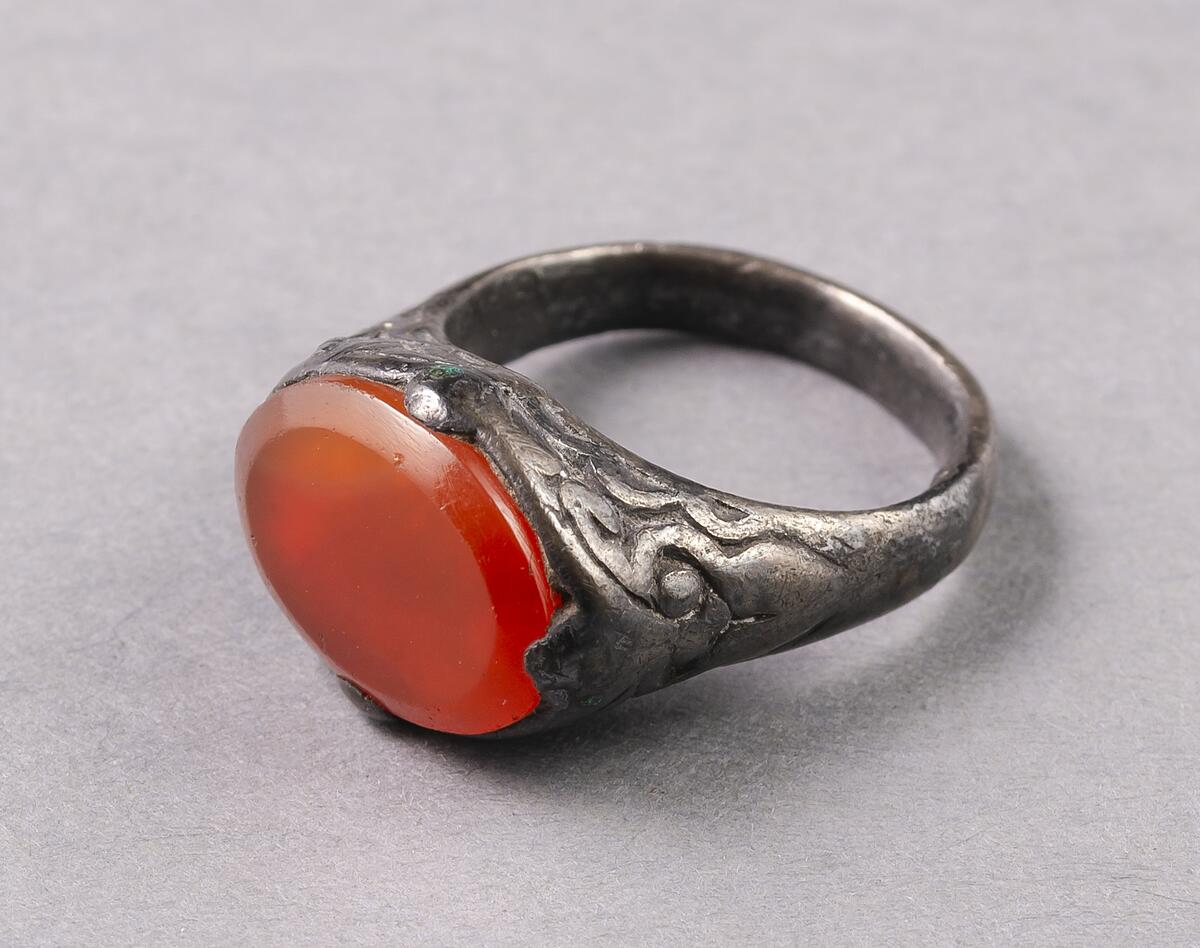 AV SILVER, MED SMAL SLÄT SKENA SAMT INFATTADE OVAL KARNEOL; INFATTNINGEN PRYDD MED VEGETATIVA ORNAMENT. STRL. 2,1 - 2,6 CM. RINGEN HAR LÄNGE VARIT I FORNSALENS ÄGO, MEN SAKNAR INVENTARIE- NUMMER. KAN MÖJLIGEN HA KATALOGFÖRTS MEN GÅR EJ ATT IDENTIFIERA.