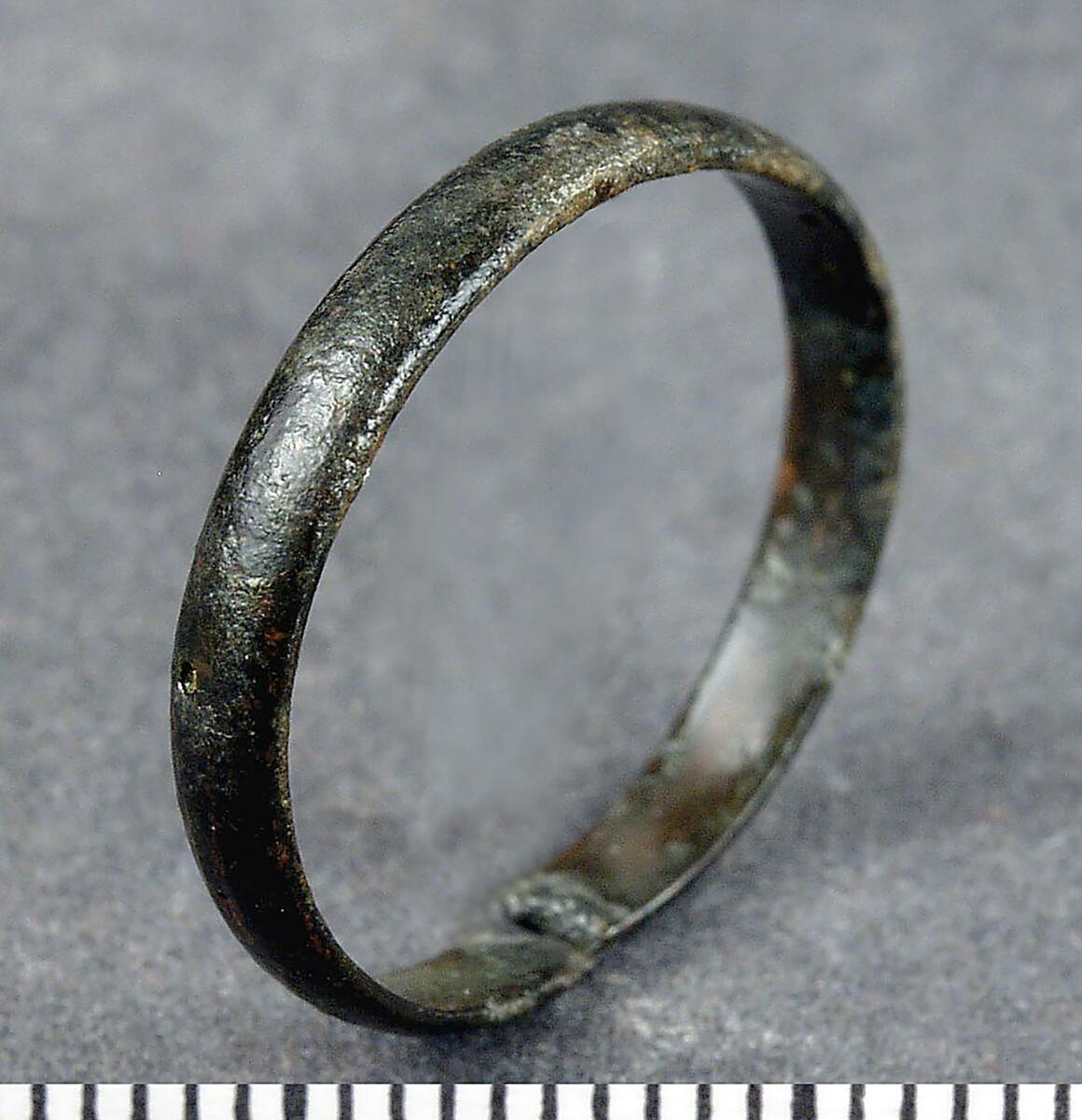 Fingerring av tunn smal bronsten, svagt välvd på utsidan, sluten modell men nu brusten på ett ställe, i övrigt se hnr c 9395:1
av brons, tunn, platt ten, löst hopfogade. Diam. 2 cm. Från hörsne kyrka.
