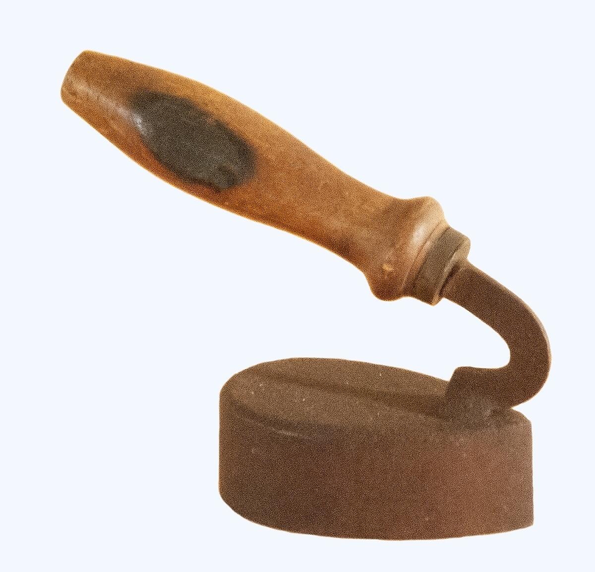 Pressjärn av järn med svarvat handtag av trä som sitter fast längst fram. Längd 15,5 cm, bredd 5 cm, höjd 13 cm. Ändrad av k.h. & s.h. Fma hgo.
av Järn, med handtag av trä. Järnets l. 10 cm. Br. 5,3 cm.