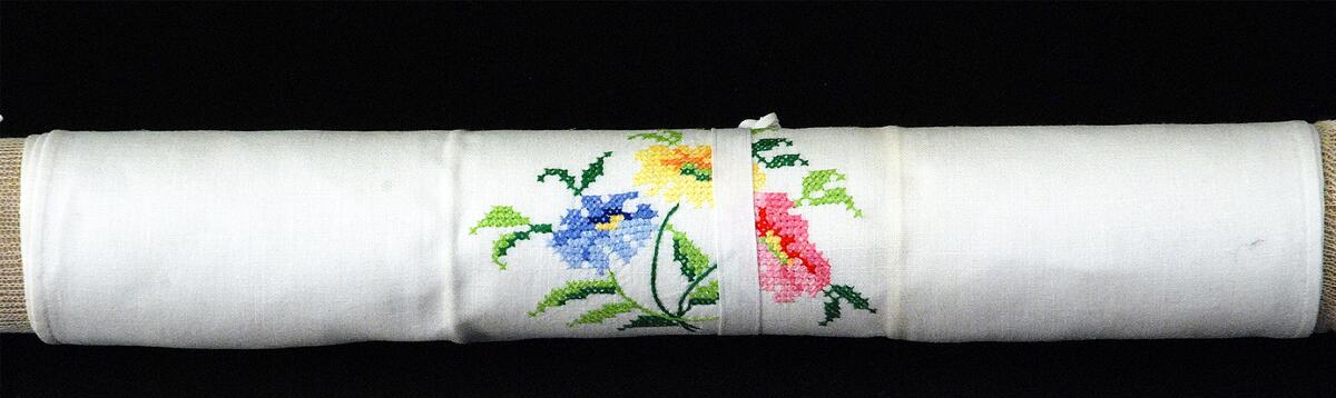Gästhandduk i vitt linne med broderade blommor. Korsstygn i rosa, rött, gult, grönt och blått, bred fåll med hålsöm. Nedre kanten rosa, hängare, en av tre handdukar i samma stil
Nyreg 020404 LI,  en del föremål från Violet Bergdahls dödsbo registrerades av någon anledning ej när det kom in till museet 1987, utan görs nu april 2002, i samband med genomgång av föremål i textilmagsinet
