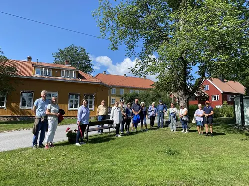 En gruppe mennesker på en gressplen foran eldre trehusbebyggelse.