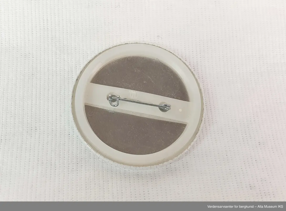 Rund hvit button i plast og metall, motivet er av en rød laks med teksten: "Varig vern av Alta-Kautokeinovassdraget! Omgjør Stortings-vedtaket".