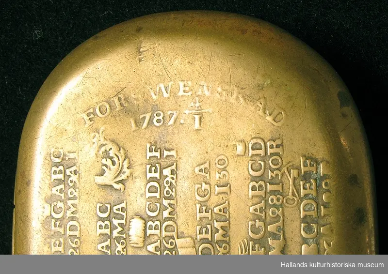 Kalenderdosa. Rektangulär med rundade hörn. På locket en kalender med bokstäver och symboler i upphöjd relief. Höger: "FORSWENSKAD 1787 4/1". Vänster: "JANUAR: FEBRUA: MARTI: APRIL: MAIUS: JUNIUS:" Mittbak på dosans kant finns ett hål.