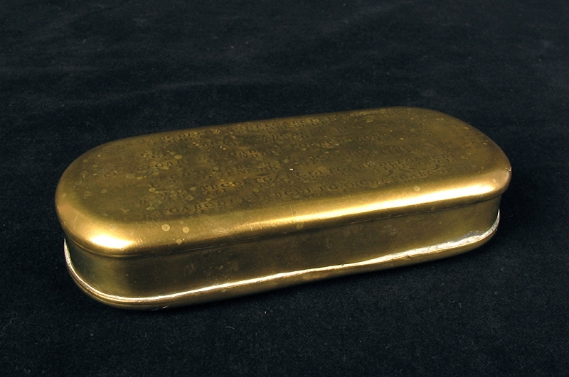Kalenderdosa. Rektangulär med avrundade hörn och fällock. På locket en kalender med bokstäver och symboler i upphöjd relief.