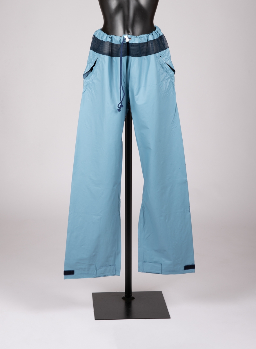 Bukse med snortrekk med stoppere i livet. Luftenetting øverst i livet. Borrelås med klaff nederst på ben. Sveisede stikklommer.