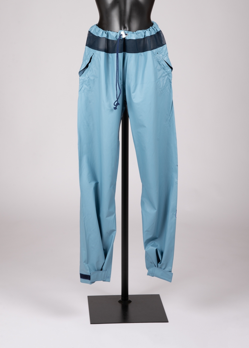 Bukse med snortrekk med stoppere i livet. Luftenetting øverst i livet. Borrelås med klaff nederst på ben. Sveisede stikklommer.