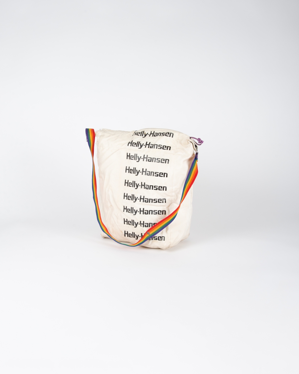 Hvit bag med skråstilte regnbuestriper. På den andre siden er det ni repiterende logoer nedover: Helly-Hansen. Glidelåslukning på toppen. Bærerem vevd i regnbuestripe på hver side festet med tre niter på forsterkningsstykke. Metallring mellom rem og forsterkningsstykke.