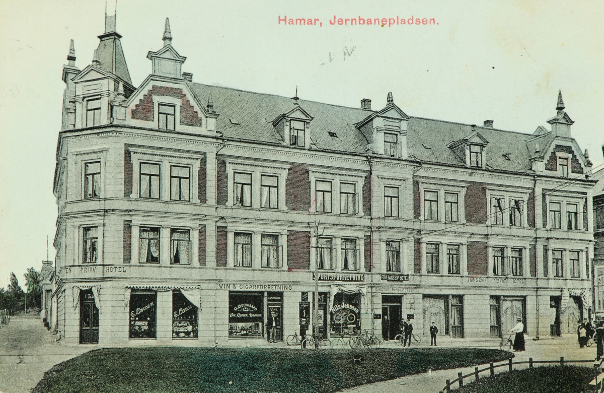 Postkort, Hamar, Jernbaneplassen, forretningsgården Torggata 3, Syver Andersens gård bygd i 1895 som han solgte i 1922 til Søndre Hedemarkens Sparebank og i 1935 kjøpte Singer Co og bygården ble kalt Singergården. E. Larsen, G. Øvergaard vin og Cigarforretning, Nils Jenssen sportsforretning, Fru Hansen`s private hotel