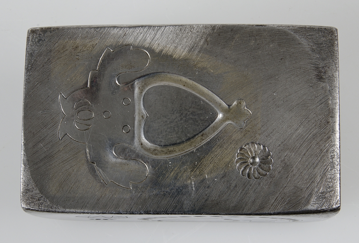 Rektangulär stans av järn till allmogebrosch. Har stansar på två sidor, till två olika broschmodeller.