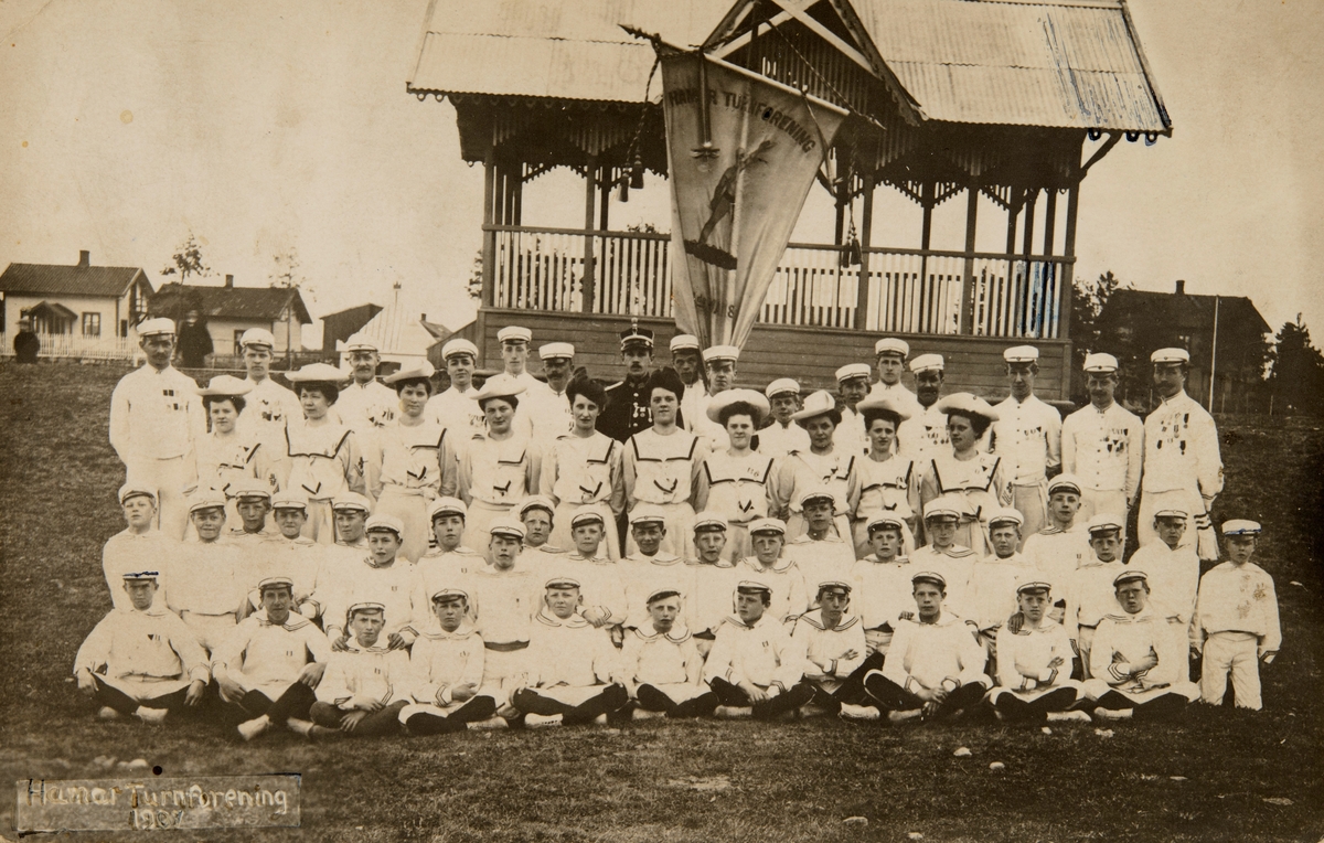 Hamar, Utstillingsplassen, Hamar turnforening, stor guppe barneturnere, gutter og jenter, kvinner og menn foran musikkpaviljongen, I forbindelse med Det 6. nasjonale turnstevnet på Hamar i 1907,