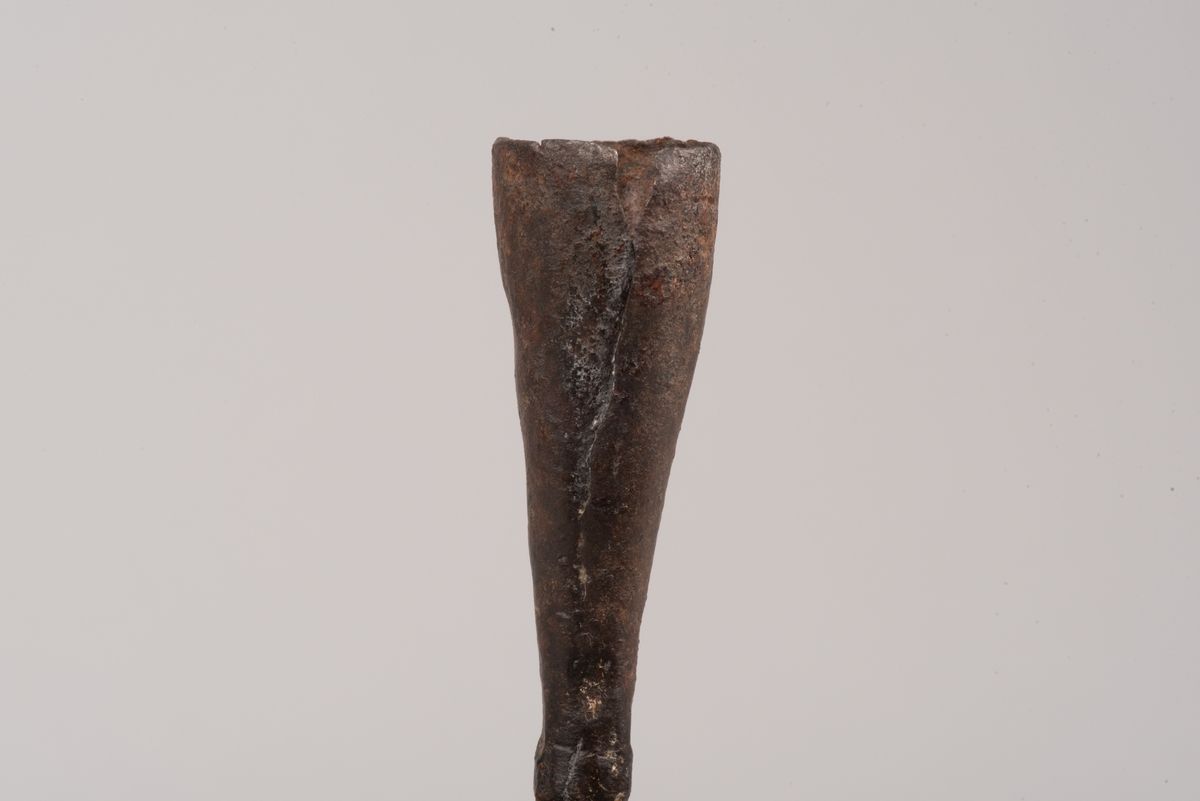 Ljusstake av järnplåt.
Ljusstake med tre fötter som har en uppvikt kant nederst och är avsmalnande uppåt. Fötterna är fästade vid en rund platta där även den smala ljuspipan sitter.
Fötterna är dekorerade med grunt inslagna cirklar som bildar en triangel med spetsarna nedåt. Kanterna är avfasade och ovanför trianglarna är kanten även markerad med några skåror.