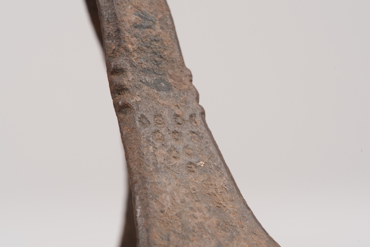 Ljusstake av järnplåt.
Ljusstake med tre fötter som har en uppvikt kant nederst och är avsmalnande uppåt. Fötterna är fästade vid en rund platta där även den smala ljuspipan sitter.
Fötterna är dekorerade med grunt inslagna cirklar som bildar en triangel med spetsarna nedåt. Kanterna är avfasade och ovanför trianglarna är kanten även markerad med några skåror.