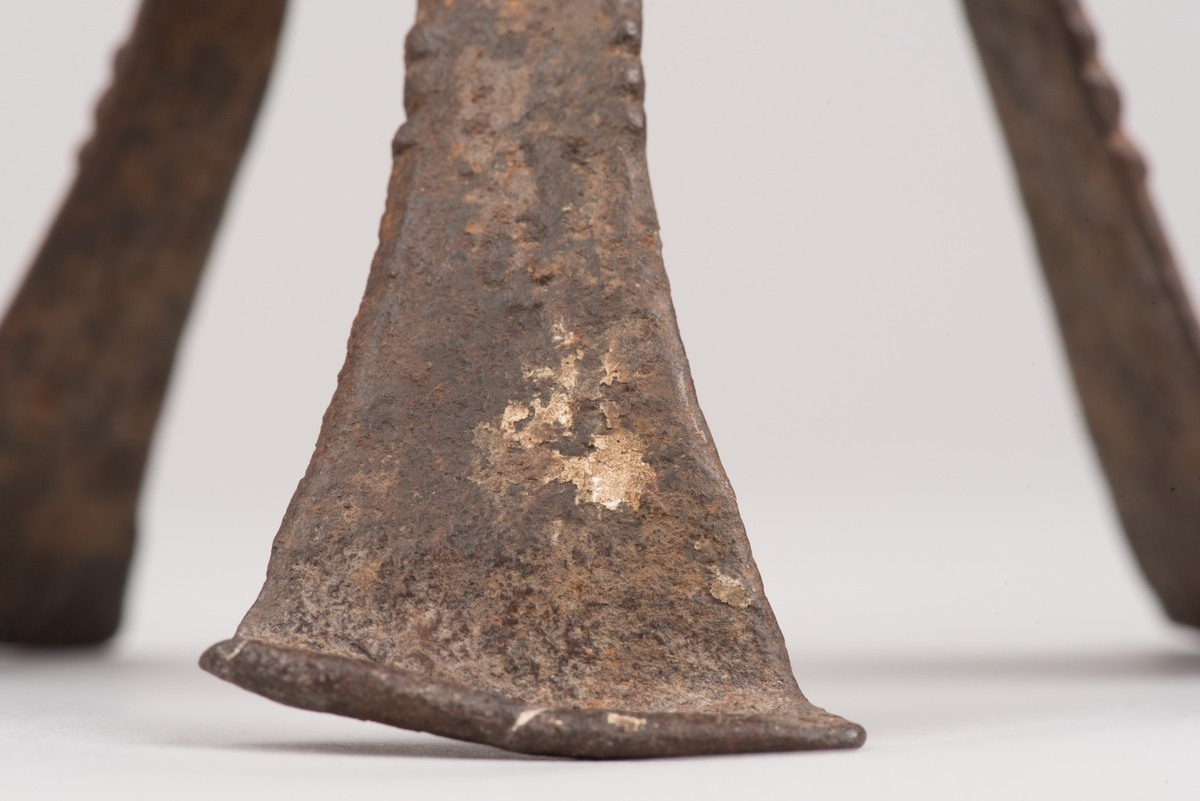 Ljusstake av järnplåt.
Ljusstake med tre fötter som har en uppvikt kant nederst och är avsmalnande uppåt. Fötterna är fästade vid en rund platta där även den smala ljuspipan sitter.
Fötterna är dekorerade med grunt inslagna cirklar som bildar en triangel med spetsarna nedåt. Kanterna är avfasade och ovanför trianglarna är kanten även markerad med några skåror.