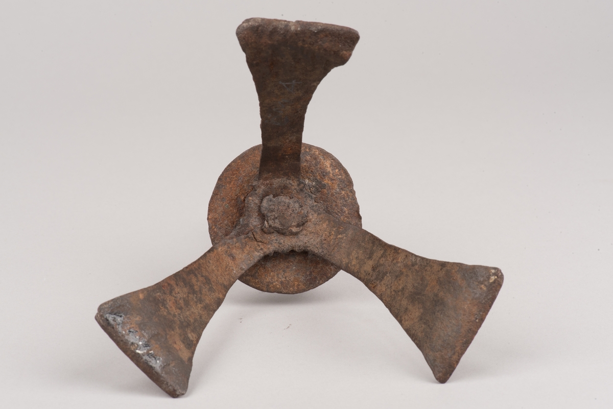 Ljusstake av järnplåt.
Ljusstake med tre fötter som har en uppvikt kant nederst och är avsmalnande uppåt. Fötterna är fästade vid en rund platta där även den smala ljuspipan sitter.
Fötterna är dekorerade med grunt inslagna cirklar som bildar en triangel med spetsarna nedåt. Kanterna är avfasade och ovanför trianglarna är kanten även markerad med några skåror.