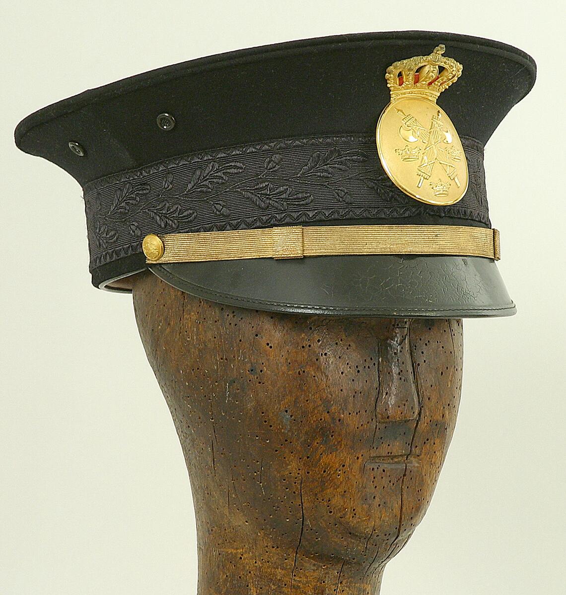 Uniformsmössa till landsfiskaluniform, hela uniformen (förutom mössan) har tidigare skänkts till museet se invnr c11695:, landsfiskal holmqvist som bodde på strandvägen 6 i visby levde 1880-1962 och uniformen skänktes av sonen, stig holmqvist, ovanstående donator, britt bolin är förmodligen också släkt, ev barnbarn till landsfiskalen,  mössan är mörkblå med svart lackskärm, guldgalon samt ovalt ämbetsmärke, krönt av krona, i metall, i fodret tillverkaretikett "pub paul u bergströms ab stockholm", till mössan hör ett skyddsöverdrag(?) i vit bomull
nyreg data 030107