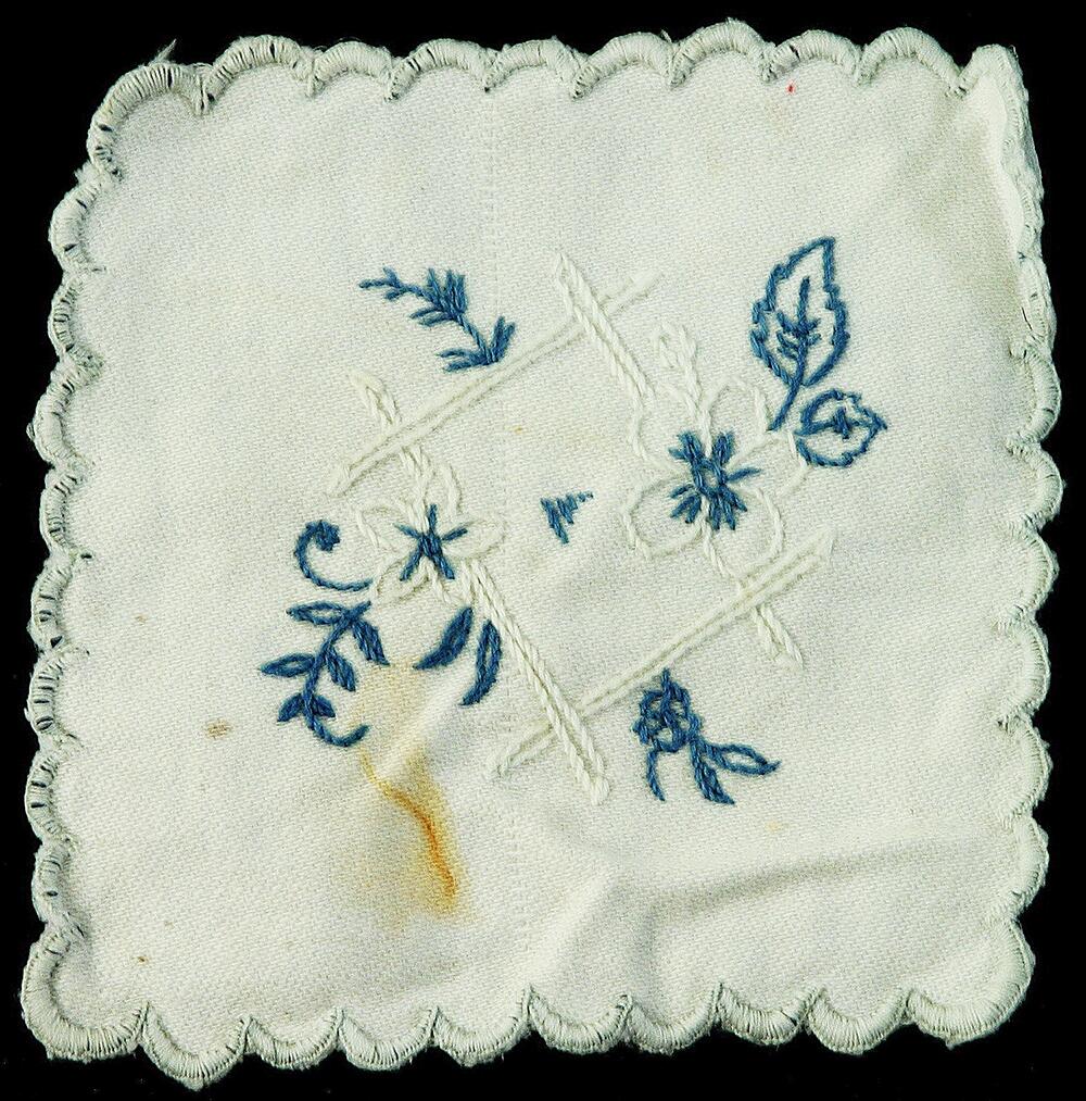 Fyrkantigt glasunderlägg i vit bomull. Broderi i blått och vitt, langettkant i vitt .
Nyreg september 2006 LJ