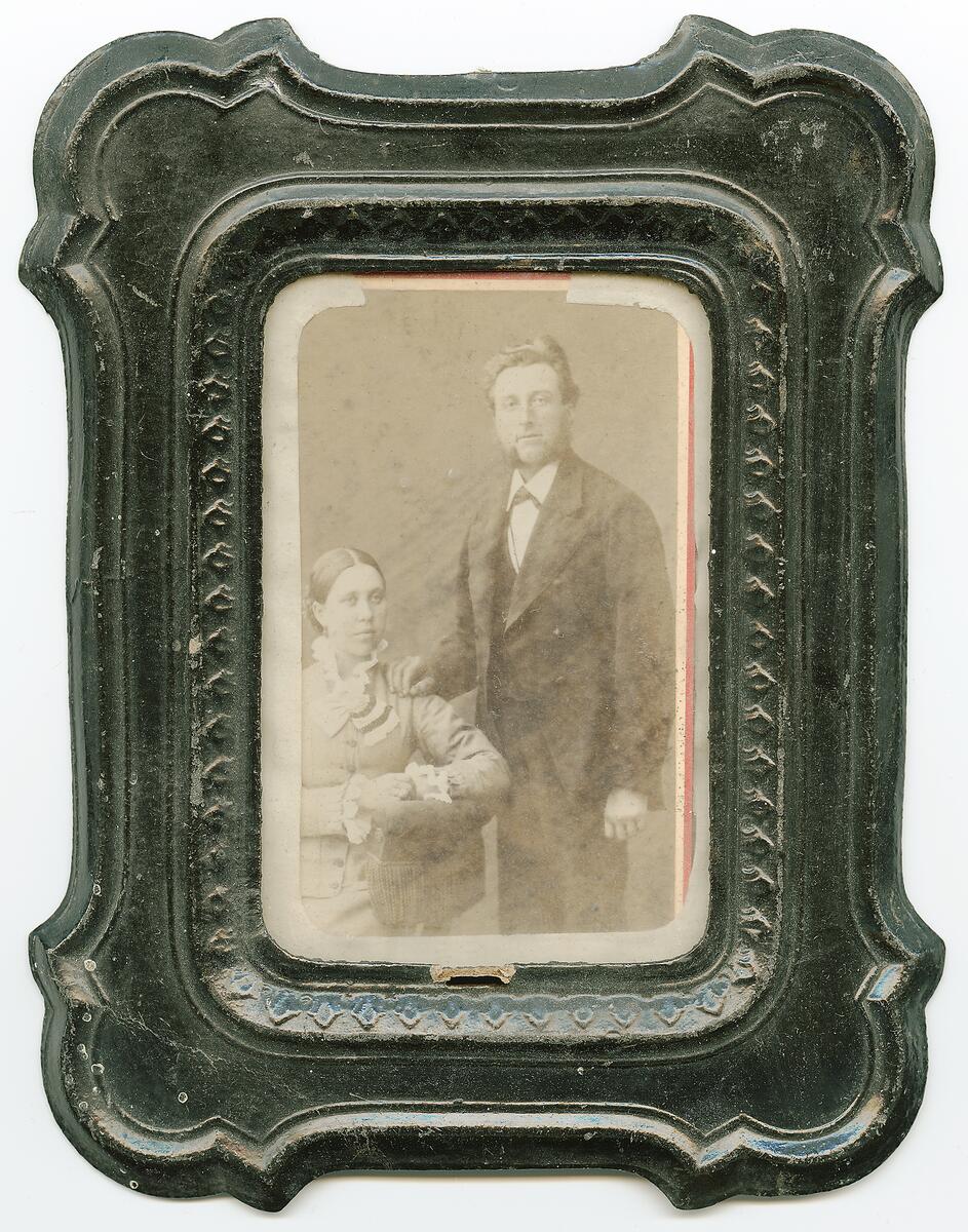 Porträttfotografi taget i ateljé Anna Lindståhl & Co, Stora Nygatan no 38, Stockholm. A L föddes 1857 och var verksam på denna adress mellan åren 1883-87.
NYREG DATA NOVEMBER  2007 LJ FOTOGRAFI FÖRESTÄLLANDE OIDENTIFIERAT PAR DÄR KVINNAN SITTER OCH MANNEN STÅR I EN RAM UTAV PRESSAT SVART PAPPER