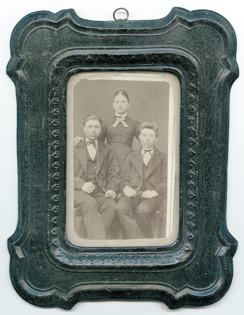 Porträtt av två okända unga män och en ung kvinna, eventuellt syskon. Bilden är tagen i N. J. A. Lagergrens fotoateljé i Klintehamn på Gotland. Lagergren, f 1843 d. 1925, var etablerad i Klintehamn under 1880-talet
NYREG DATA NOVEMBER  2007 LJ ETT FOTOGAFI FÖRESTÄLLANDE TVÅ UNGA HERRAR SITTANDE OCH EN UNG DAM STÅENDE BAKOM  KORTET KAN VARA TAGET OMKRING ÅR 1900 RAMEN ÄR FORMPRESSAD I I SVART PAPP.