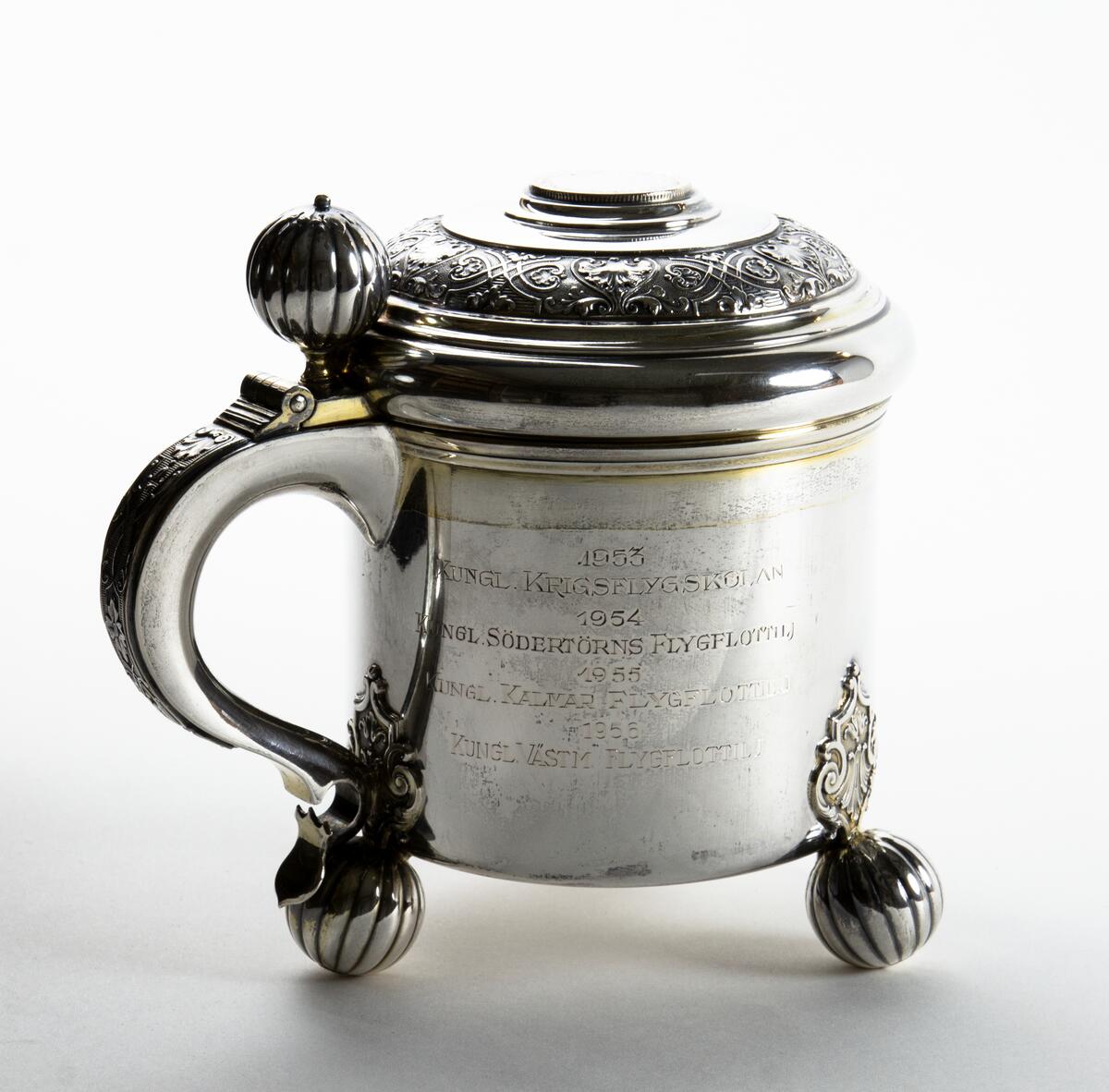 Kanna i silver Prispokal; dryckeskanna i silver Kannan står på tre kulfötter och över fästena för kulfötternafinns en utsmyckning. Tumgreppet som sitter på locket är kulformat. i lockets mitt finns ett mynt, på myntet står det: GUSTAF V SVERIGES KONUNG MED FOLKET FÖR FOSTERLANDET Runt lockets kant finns en utsmyckning. På kannan står det: SAAB SVENSKA AEROPLAN-AKTIEBOLAGET VANDRINGSPRIS FLYGVAPENMÄSTERSKAPEN PISTOL 1948 KUNGL. JÄMTLANDS FLYGFLOTTILJ 1949 KUNGL. VÄSTM. FLYGFLOTTILJ 1950 KUNGL. VÄSTM. FLYGFLOTTILJ 1951 KUNGL. SÖDERM. FLYGFLOTTILJ 1952 KUNGL. SKARAB. FLYGFLOTTILJ 1953 KUNGL. KRIGSFLYGSKOLAN. 1954 KUNGL. SÖDERTÖRNS FLYGFLOTTILJ 1955 KUNGL. KALMAR FLYGFLOTTILJ 1956 KUNGL. VÄSTM. FLYGFOLOTTILJ. Kannan är opolerad.