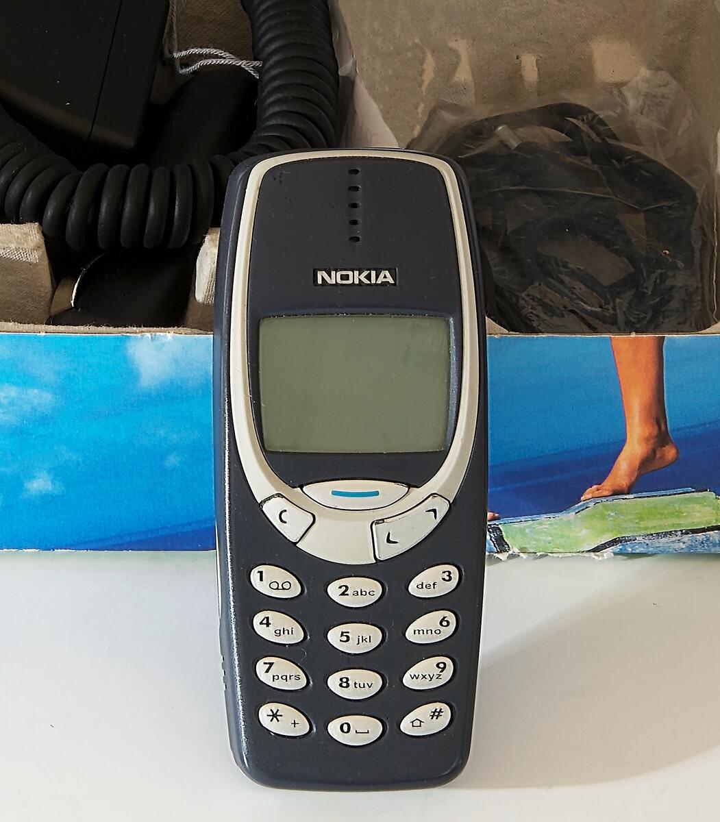 Nokia mobiltelefon modell 3310. Skal av mörkblått plast med silverfärgade knappar och rektangulär display. I originalkartong med laddare, billaddare, instruktionsbok och inköpskvitto.