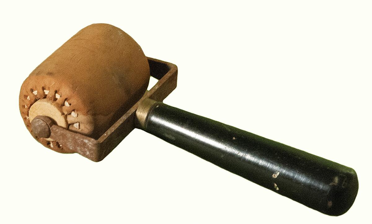 Läskpress (?). Trä, metall och läder. Rulle i trä, klädd med ljusbrunt läder. Handtag i svärtat trä. Fäste i metall mellan handtag och rulle, rostigt. 1900-talets första hälft.
Nyreg 20130215 JE