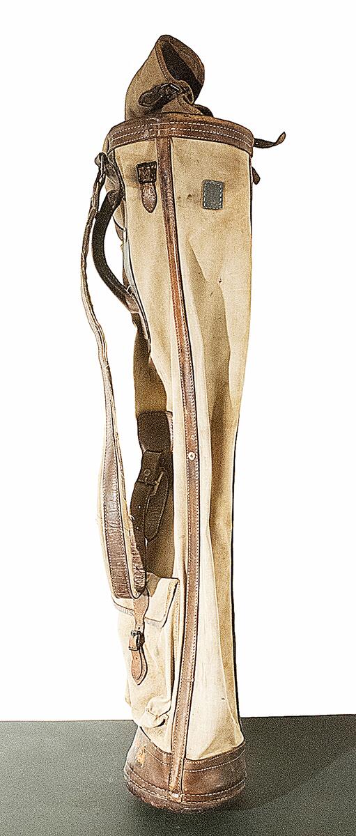 Golfväska. Beige canvas med läderförstärkta sömmar och botten. Cylindrisk form med lock samt justerbar axelrem. Framsida med förslutbar ficka för golfbollar. Under handtaget en plakett med texten "Spalding" m.m. Märkt "J.A.E.R." för John (Johnny) Albert Emanuel Roosval på väskans framsida. Tidigt 1900-tal.
Nyreg 20130219 JE