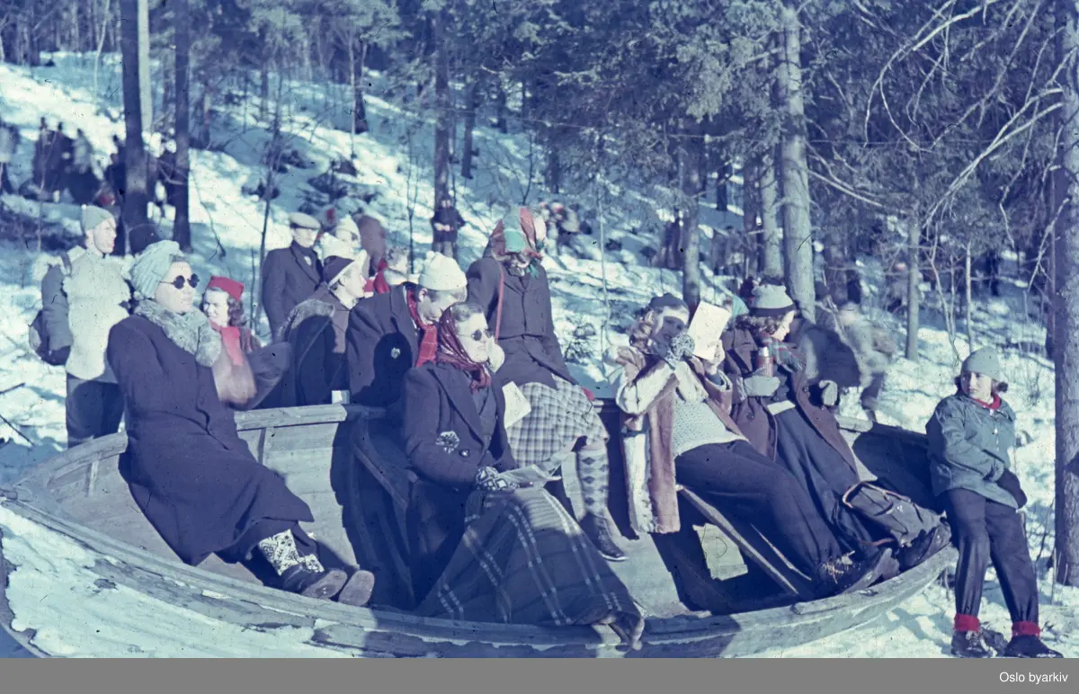 Folkemengde som ser på mest sannsynlig skirenn. Seks kvinner sitter i en båt.